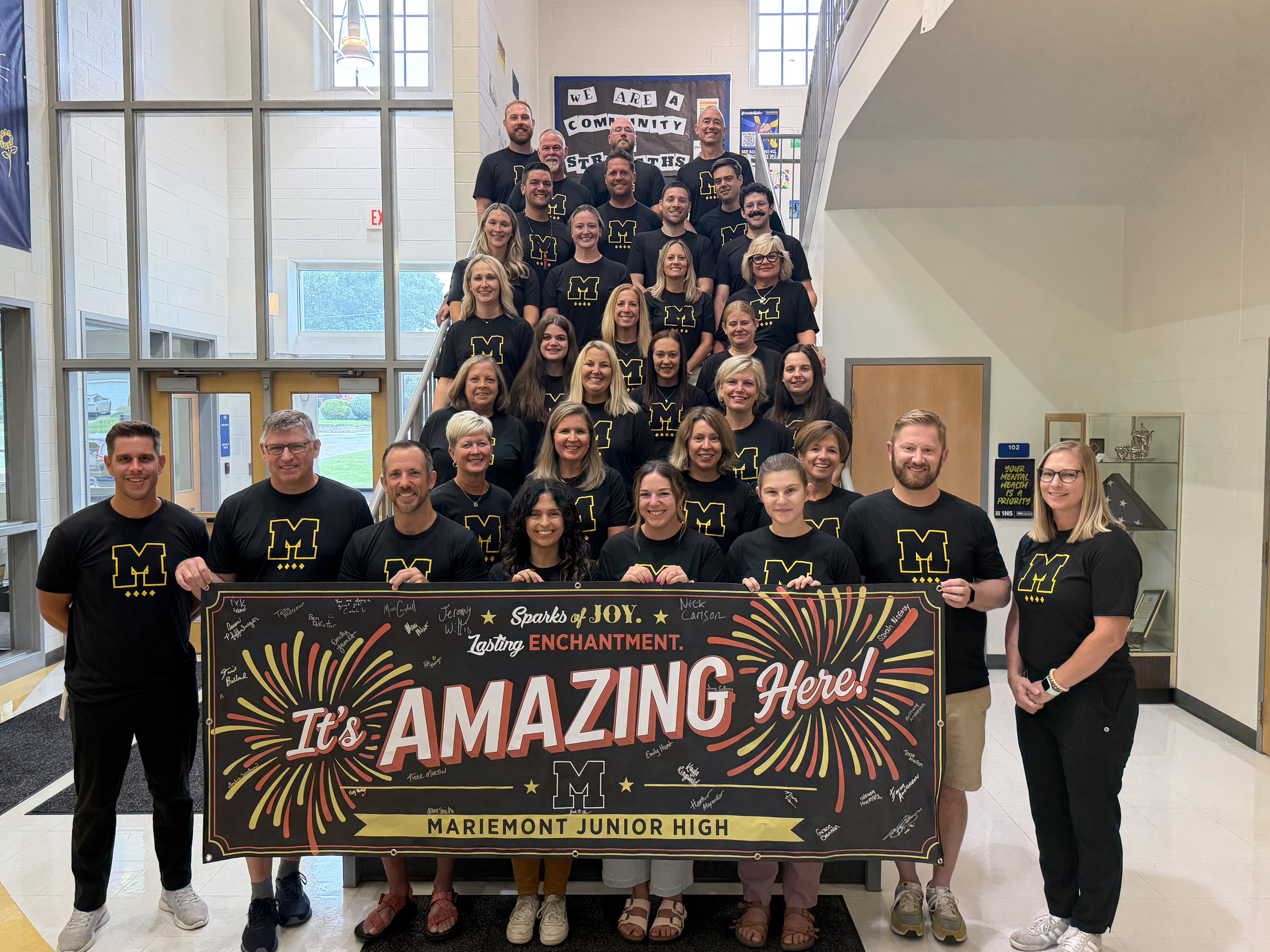 The entire Mariemont Junior High School staff poses in matching shirts with a banner that reads "It's Amazing Here!"