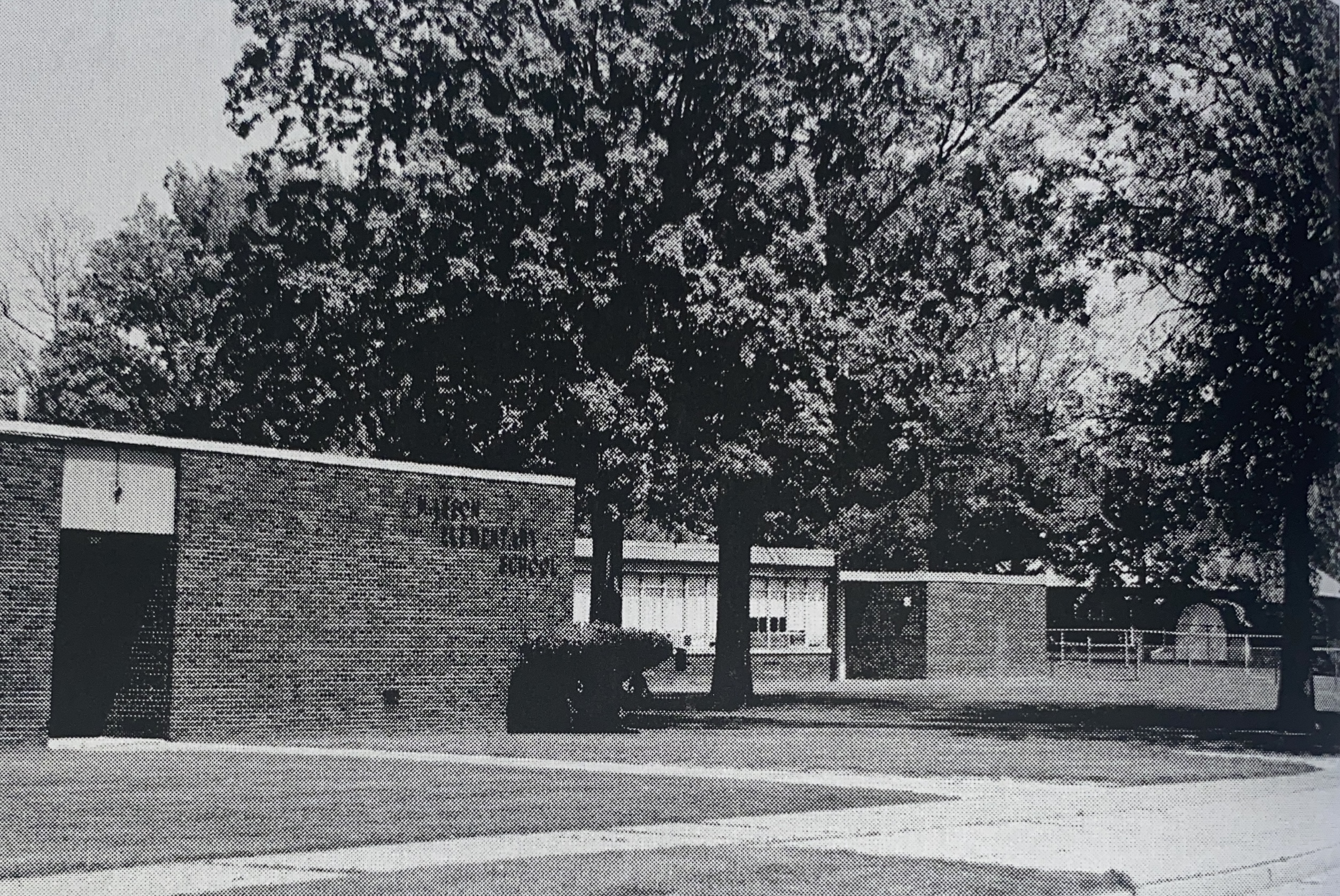 black and white photo of school building with trees surrounding 