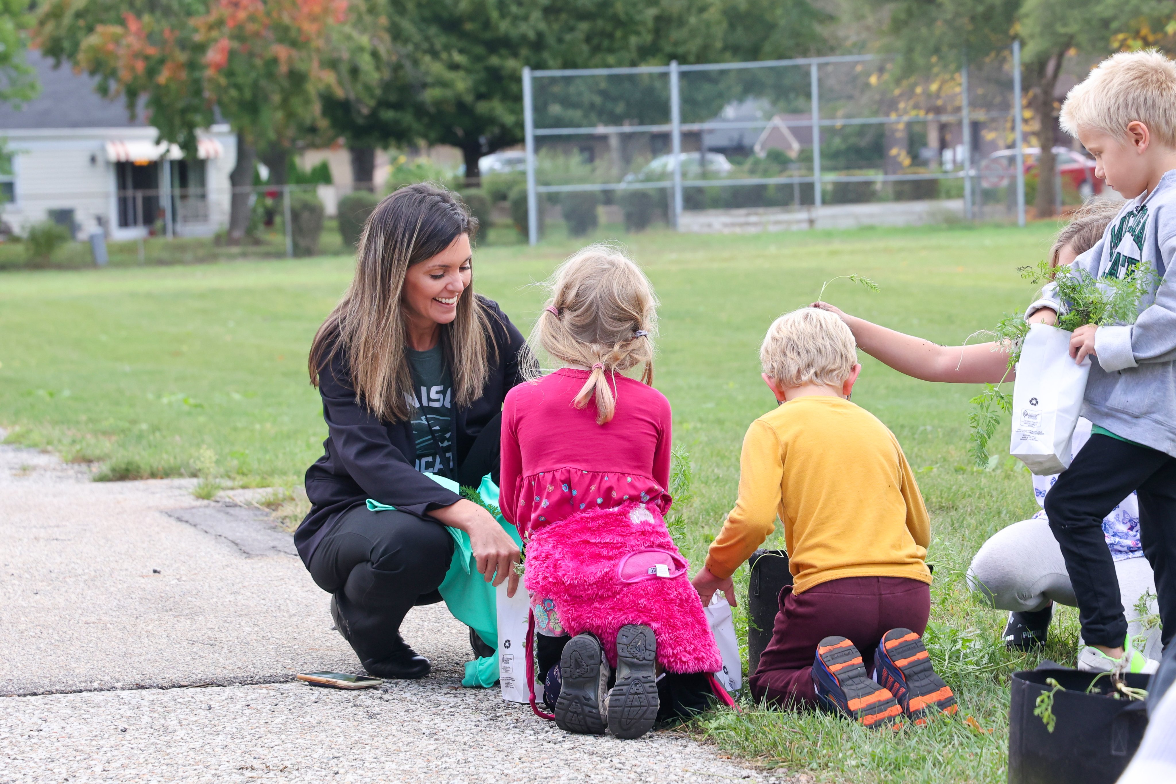 A teacher collects vegetables with students from the community garden.