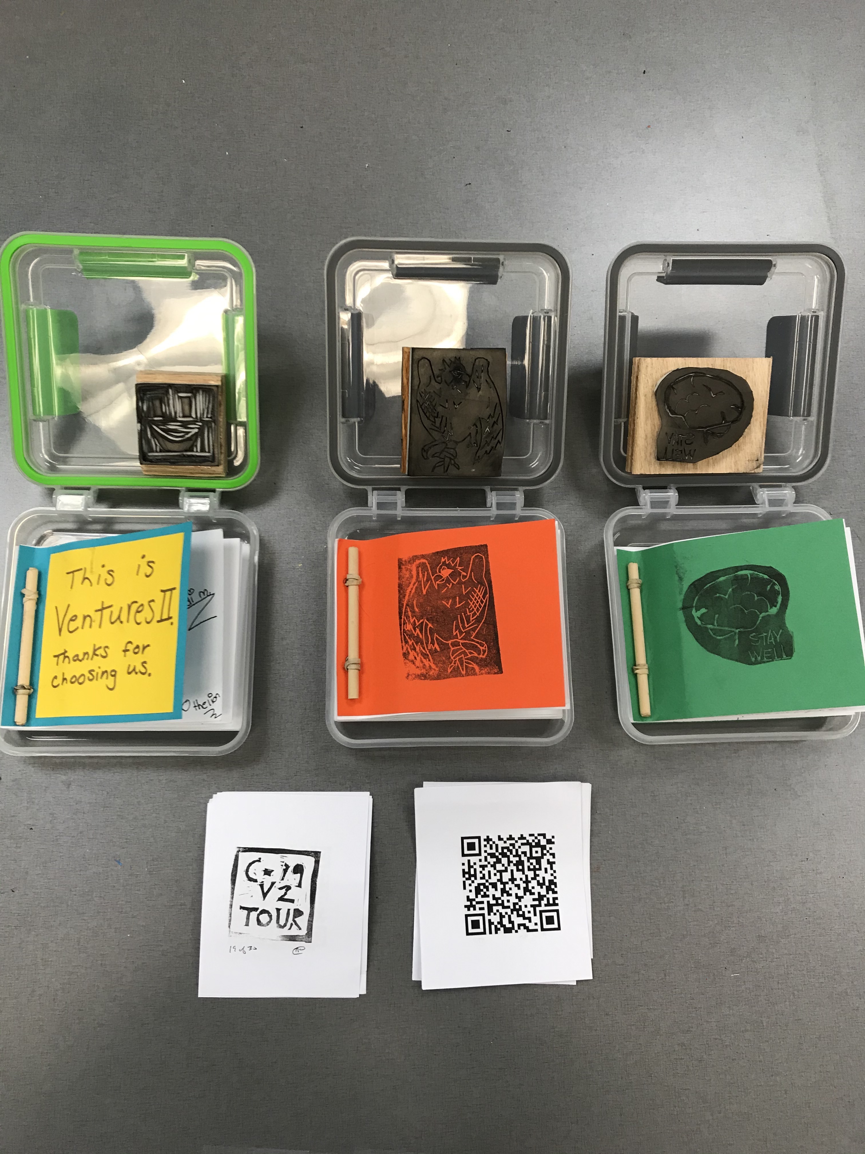 Three plastic boxes opened displaying their contents. Items include rubber stamps, paper booklets and QR codes. 
