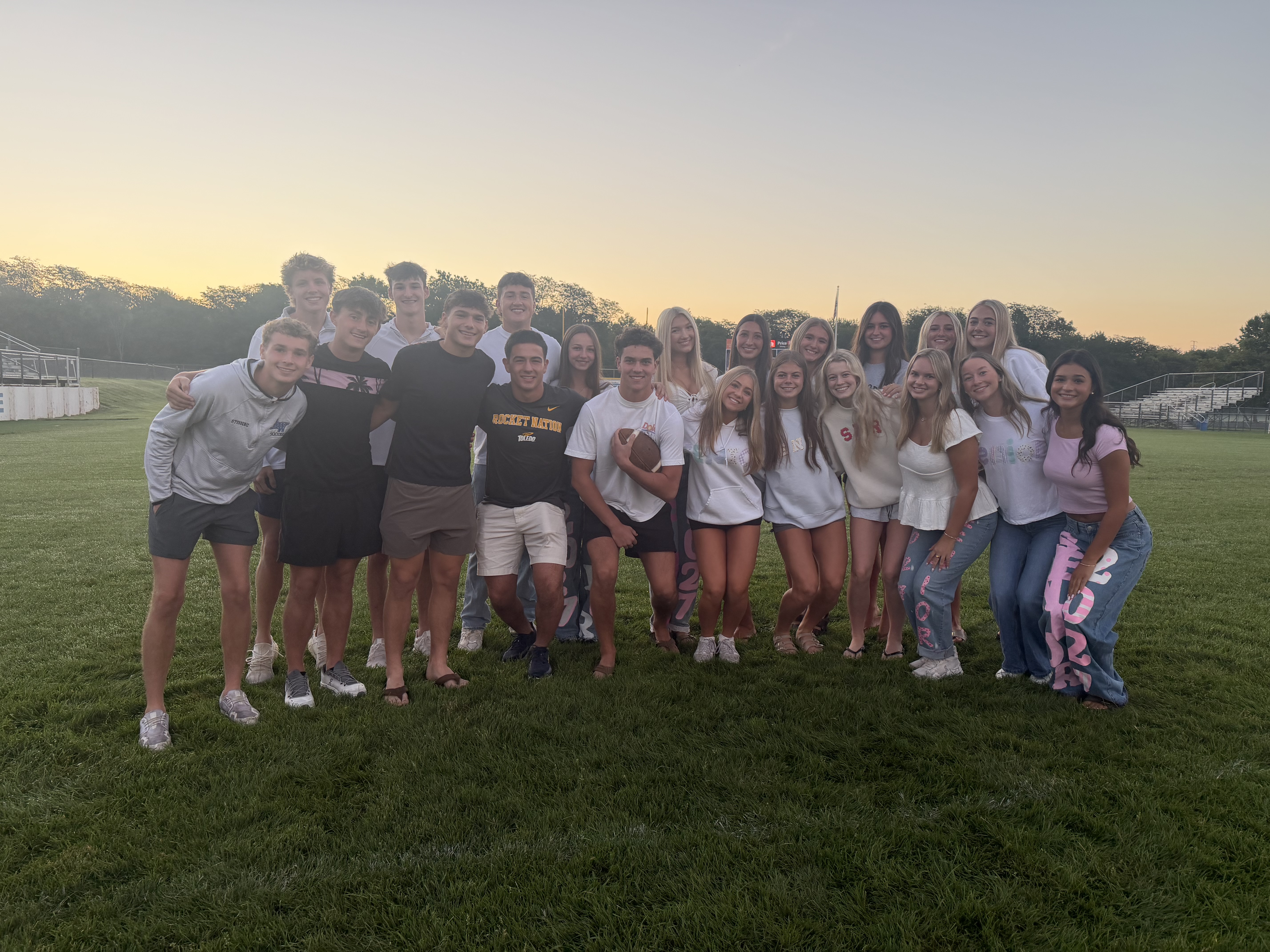 A group of students stands on the football field at dawn