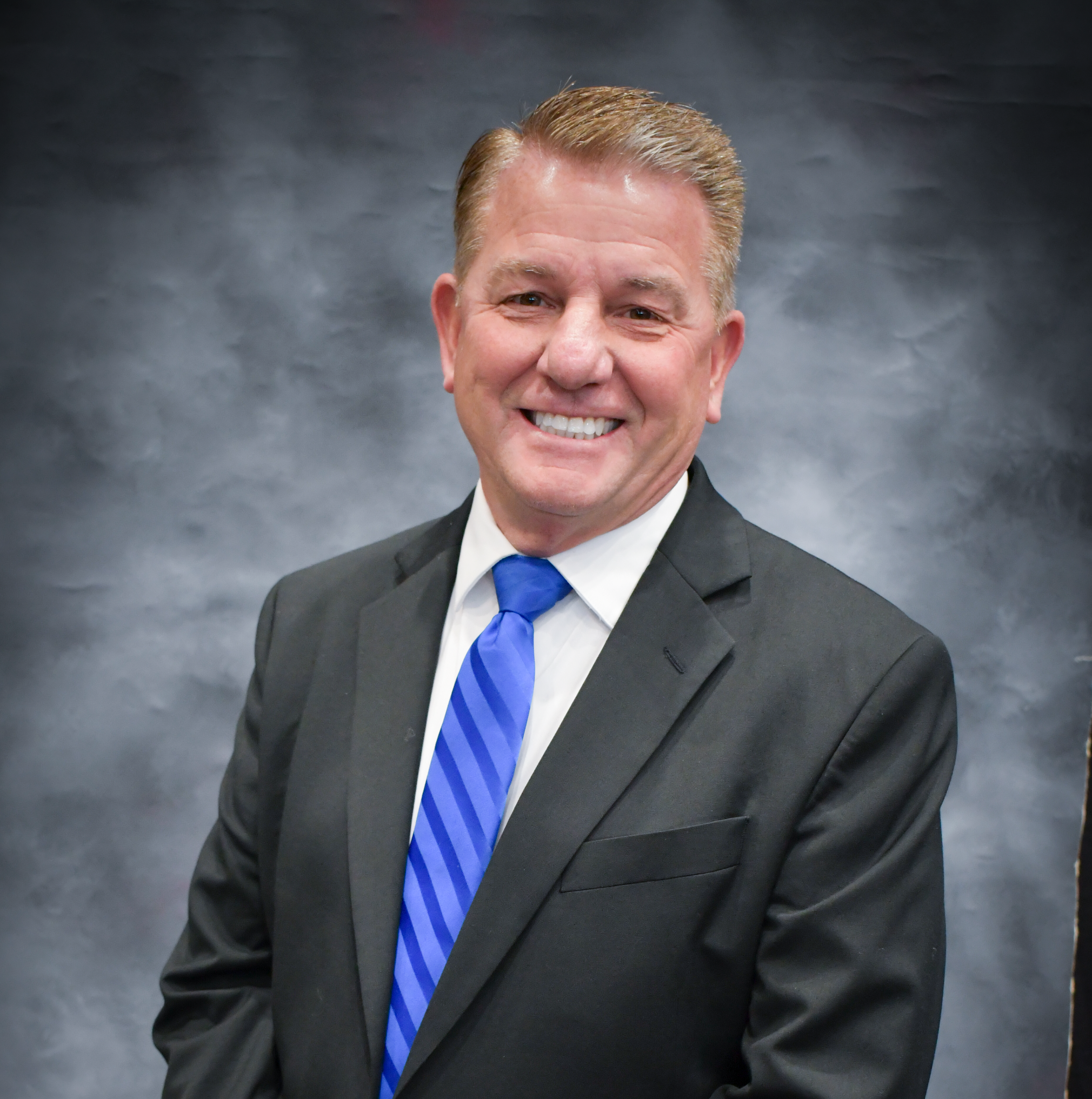 A man wearing a black suit with blue tie.