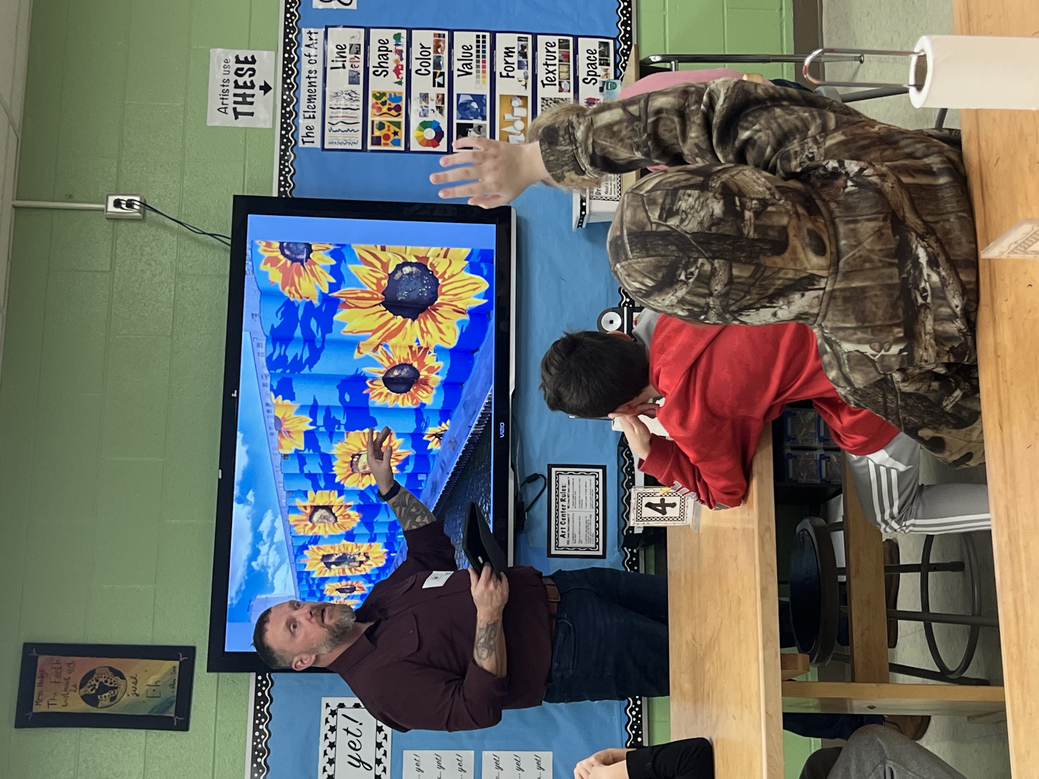 a man points at art on a tv screen while a child raises his hand