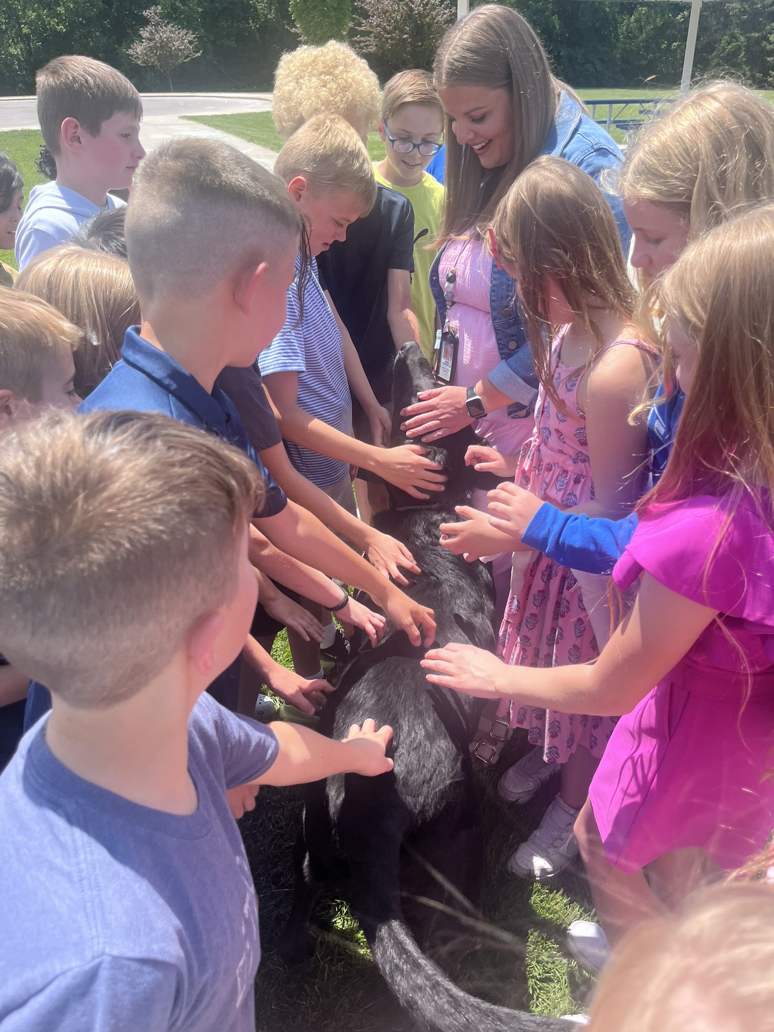A group of students and their teacher pet a black dog