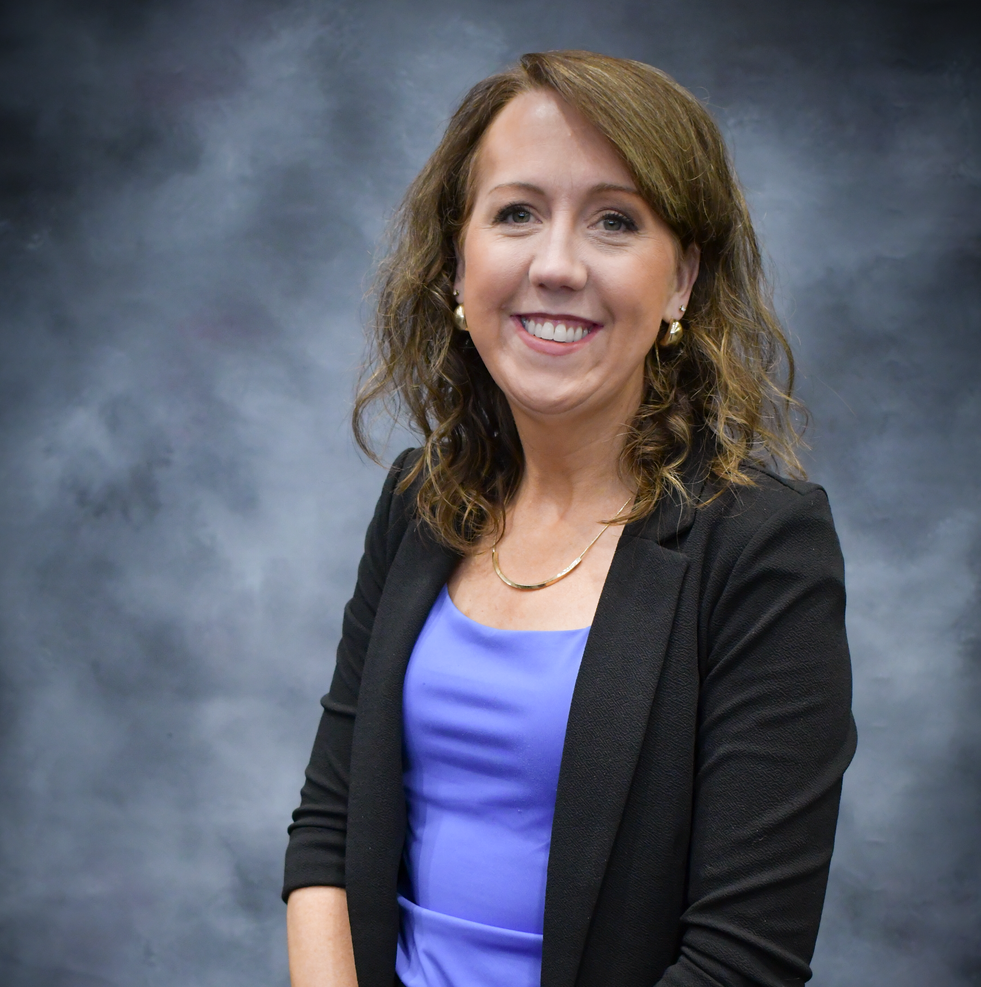 Woman with brown hair wearing a blue shirt and black blazer