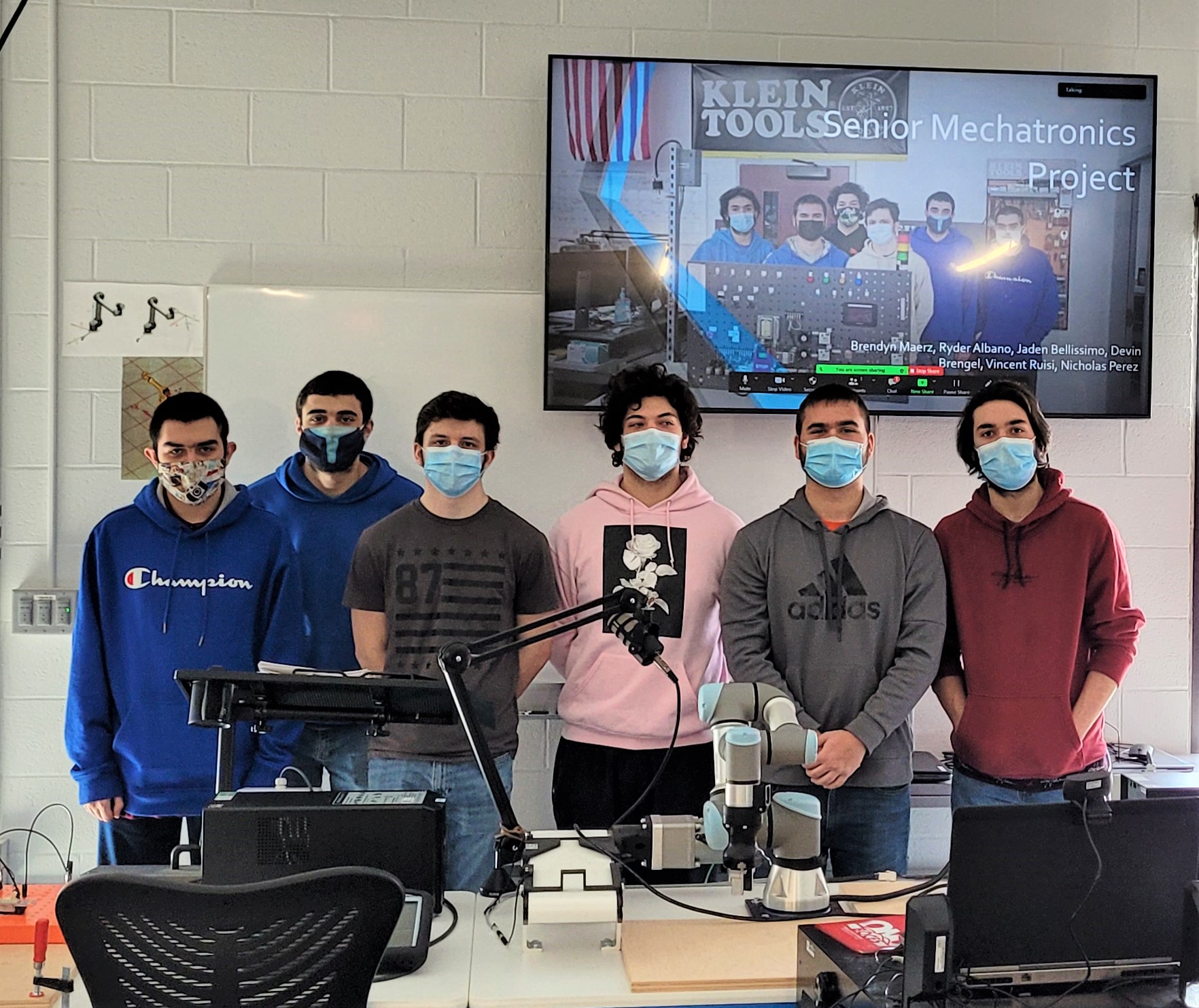 6 mechatronics students stand in front of a TV projecting their Powerpoint portion of the capstone project.