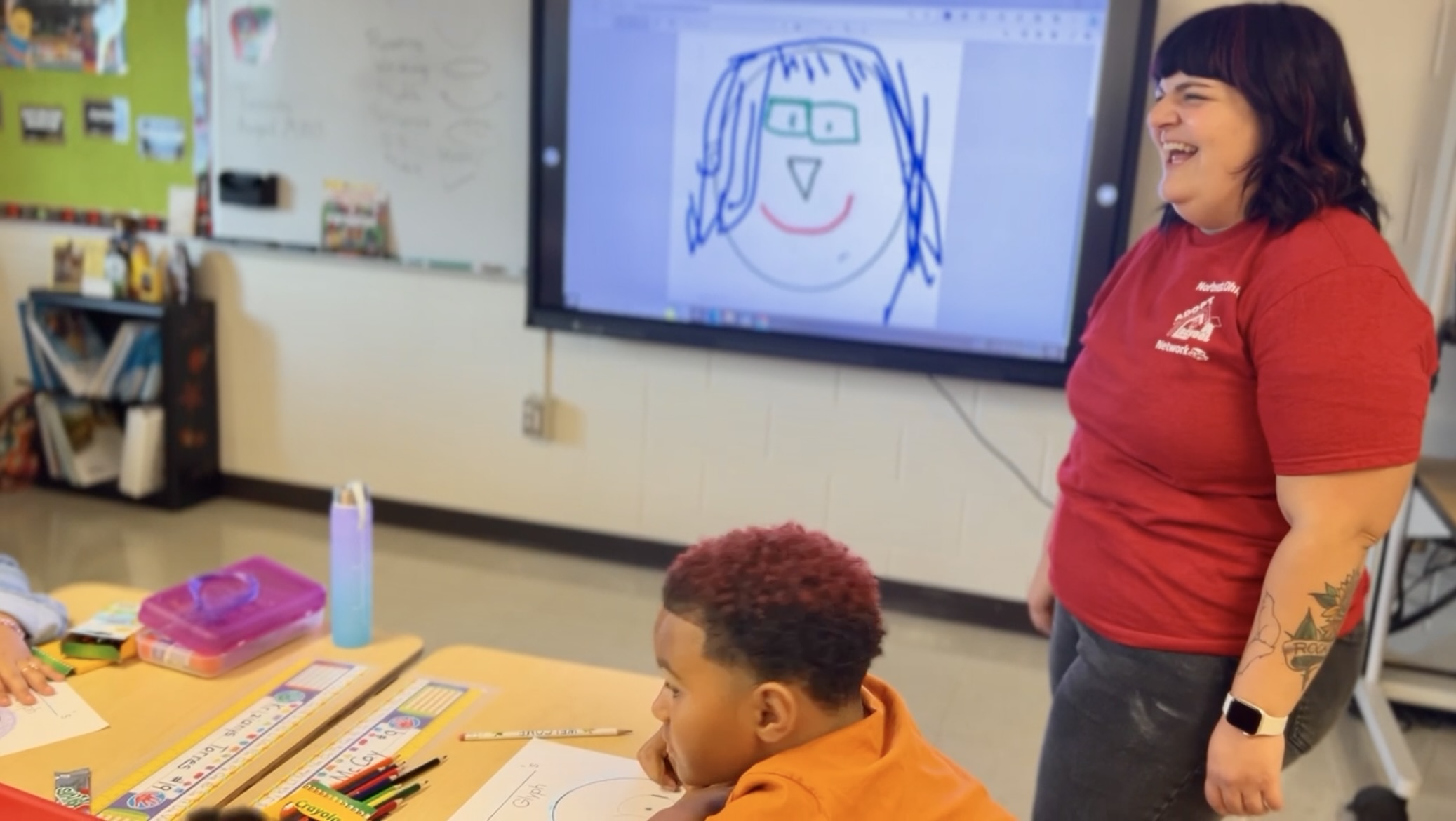 woman in red shirt smiles. standing in classroom