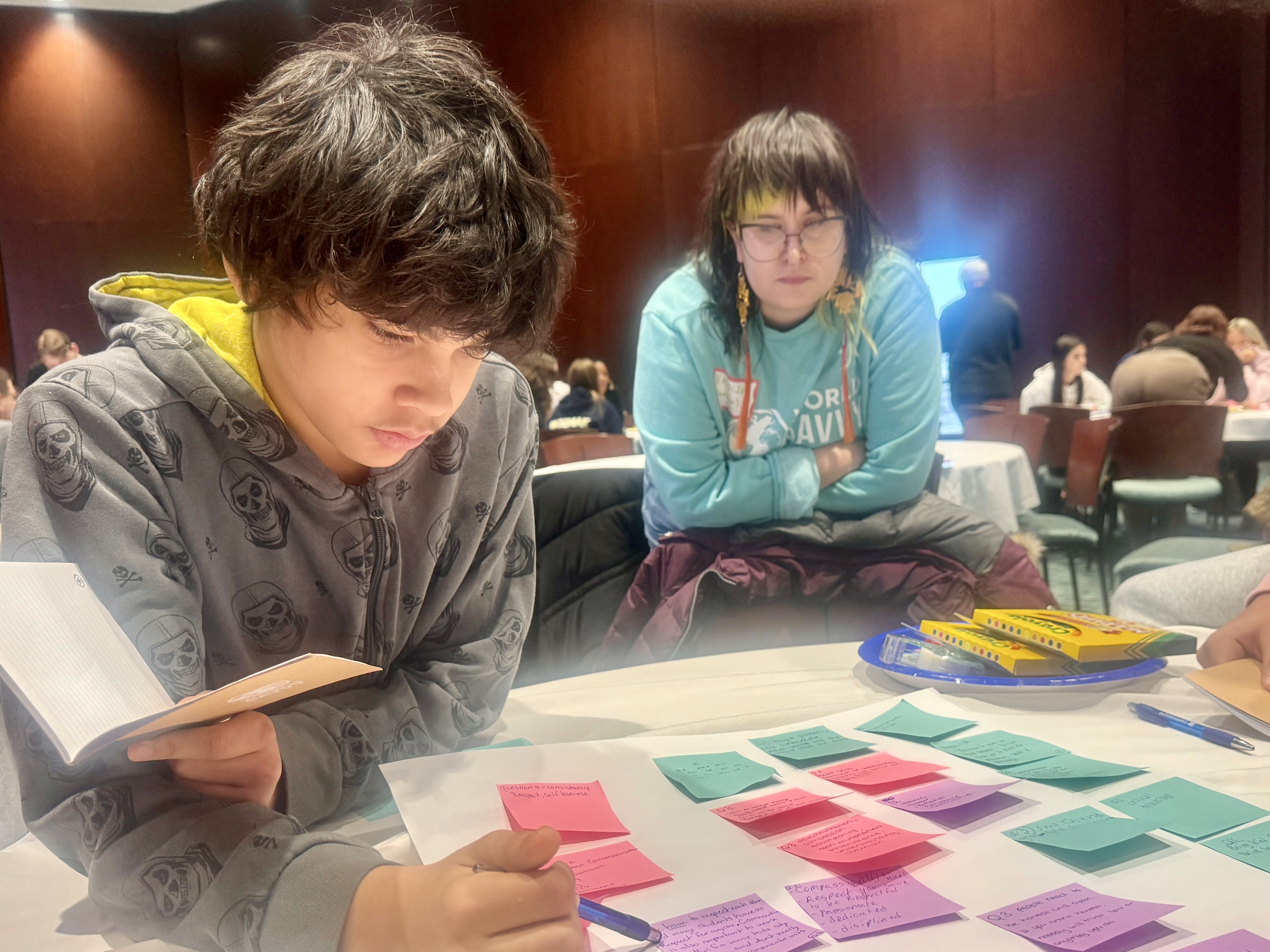 student looks at post-it notes on white board with woman looking over his shoulder in background.