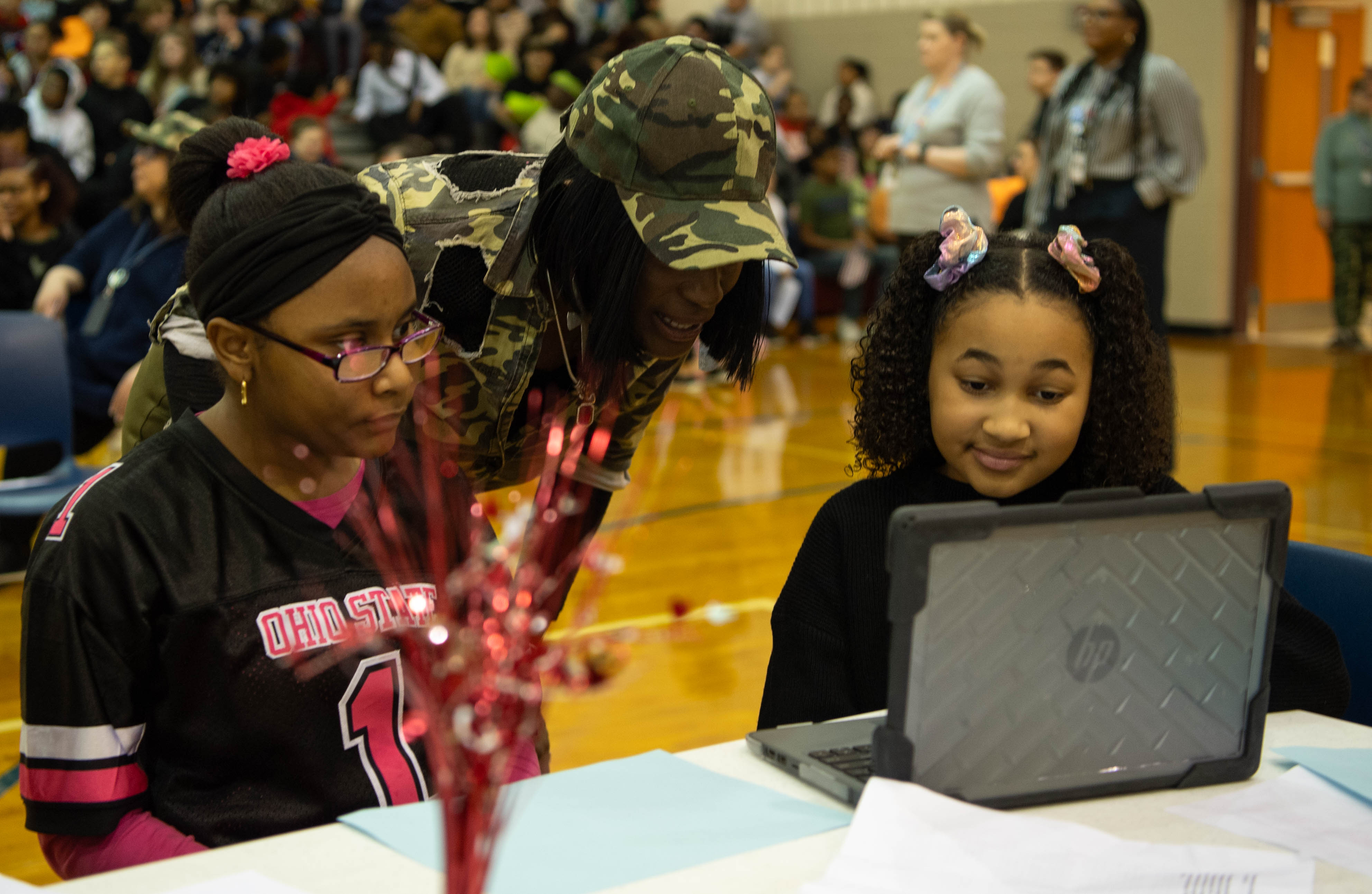 two female students and principal look at computer screens together during trivia game