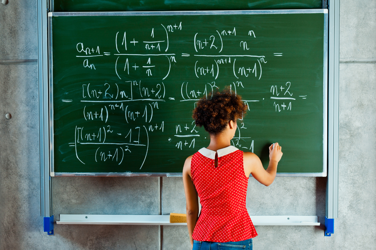 Woman writing math equations on a green chalkboard.